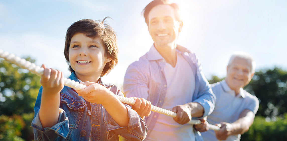 Gesundheit in der Familie Ein Junge, sein Vater und sein Großvater ziehen gemeinsam an einem Seil.
