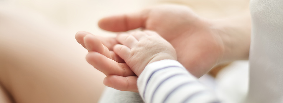 Wenn das Baby Schnupfen hat, machen sich Eltern oft Sorgen. Kleine Babyhand liegt in der Hand eines Erwachsenen.