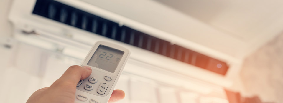 Klimaanlagen im Büro sollten nicht zu kalt eingestellt werden. Eine Person stellt mit einer Fernbedienung die Klimaanlage im Büro ein