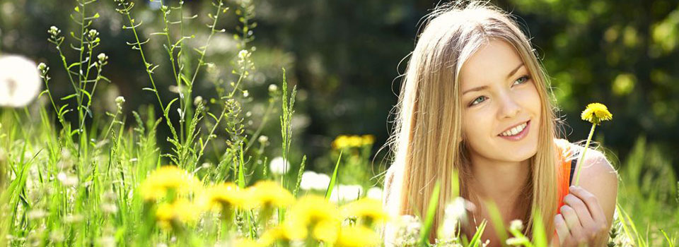Heuschnupfen-Patienten können die Natur nicht unbeschwert genießen. Eine junge Frau liegt in einer blühenden Wiese und hält eine Blume in der Hand.
